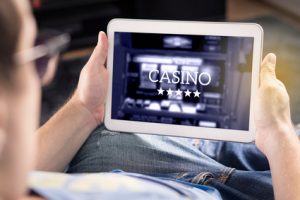 Man playing in an online casino with tablet. Modern gambling application. Slot machine app. Person holding smart mobile device in hand at home.